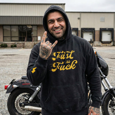 Man wearing a black hoodie with yellow text standing next to a motorcycle.