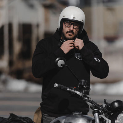 Man wearing a black hoodie with a brand logo, sitting on a motorcycle.